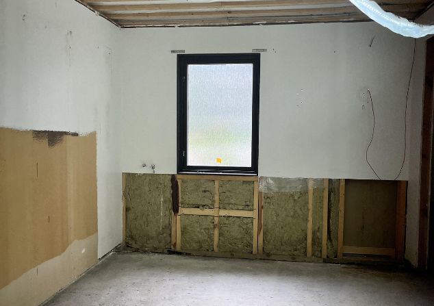 Ett tomt rum med ett fönster och isolering under fönstret på väggen.